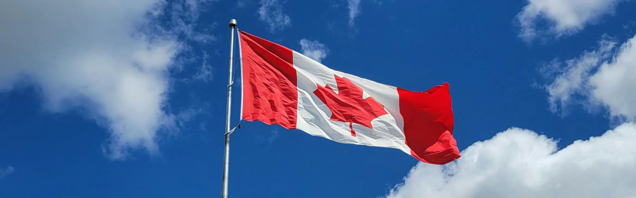 Canadian flag waving in a blue sky with fluffy white clouds